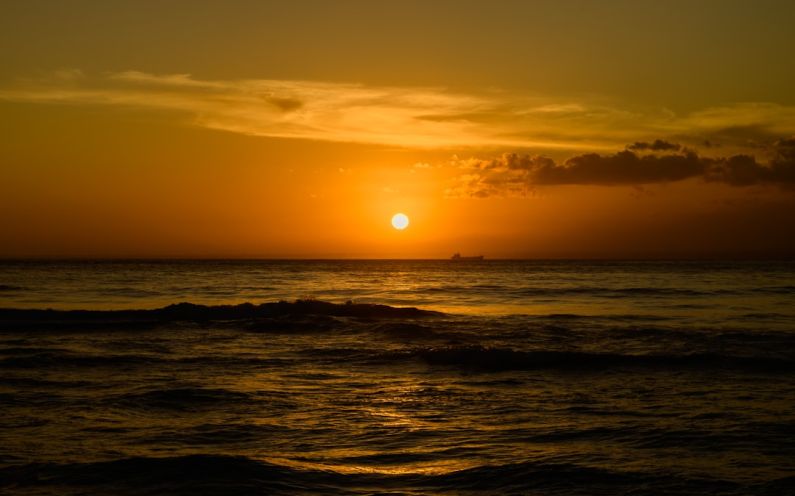 Secret Beach - a sunset over the ocean with a boat in the distance