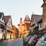 Europe Travel - white and pink petaled flowers on metal fence near concrete houses and tower at daytime