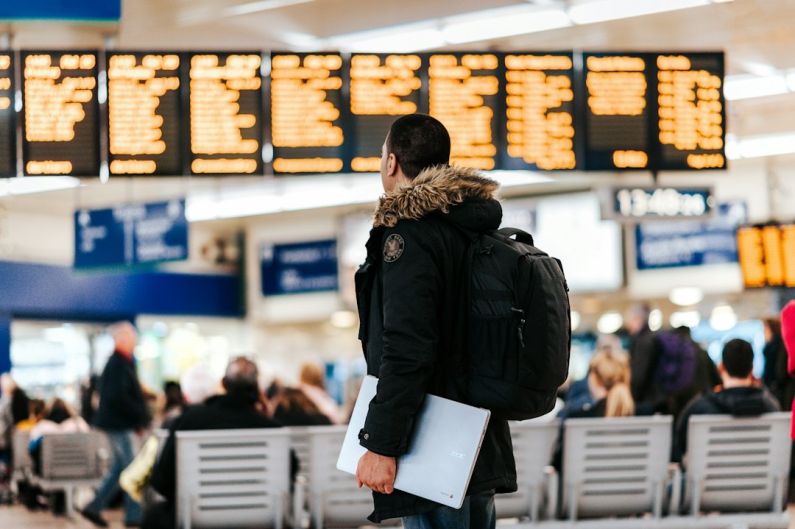 Travel Insurance - man standing inside airport looking at LED flight schedule bulletin board